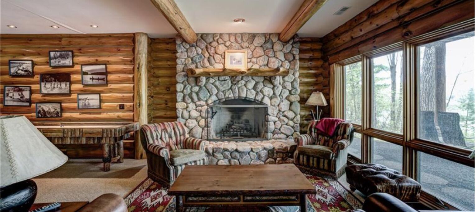 Un intérieur rustique avec une cheminée en pierre, des murs en bois et des tableaux encadrés.