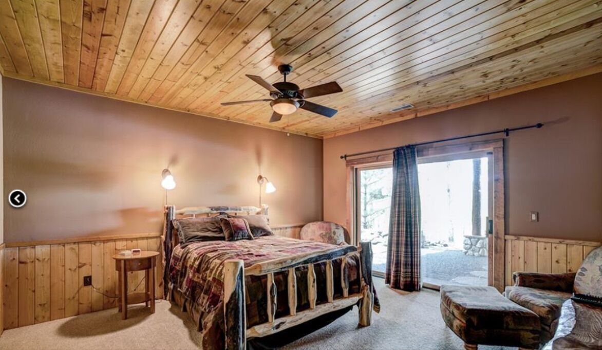 Un dormitorio con techo de madera, una cama con colcha estampada, dos lámparas de noche y vistas al exterior a través de una puerta corrediza de vidrio.