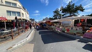 Un mercado callejero con puestos que venden diversos productos, un café y un edificio con un letrero que dice "RETOIR".