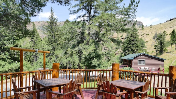A wooden deck with tables and chairs, overlooking a forested hillside and a cabin.