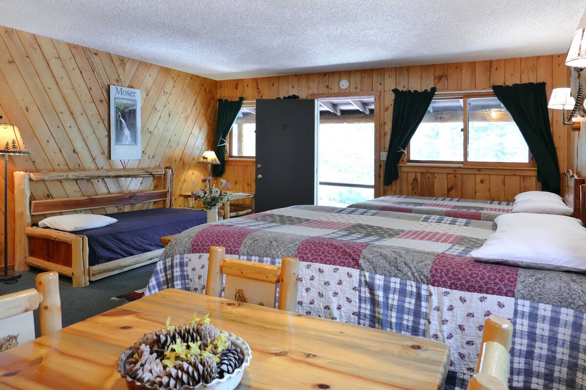 Una habitació acollidora d'estil cabana amb dos llits, una taula de dinar de fusta i una petita cuina.