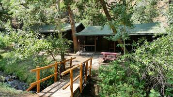 A rustic cabin with a wooden deck and a small stream nearby.