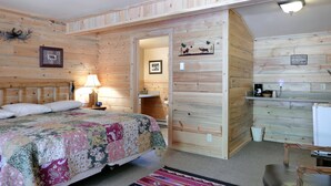 A wooden cabin with a bed, a desk, and a kitchenette.