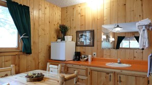 A wooden cabin interior with a dining table, chairs, a refrigerator, a sink, and a mirror.