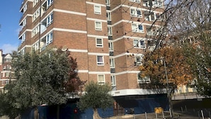 Un immeuble résidentiel à plusieurs étages, doté d’une façade en briques, de nombreux balcons et surplombant un ciel dégagé.