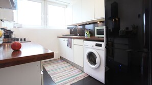 Une cuisine moderne avec des meubles blancs, un réfrigérateur noir, un lave-linge et un four à micro-ondes.