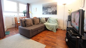 Un salon moderne avec un canapé gris, un plancher en bois, une grande fenêtre et un téléviseur.
