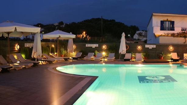 Una piscina con sillones de playa y sombrillas, rodeada por un muro bajo y plantas en macetas.