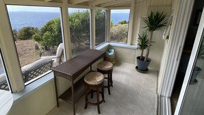 A covered patio with a table and two stools, large windows with ocean views, and potted plants. - Water Island Cottage with a View  (St Thomas)