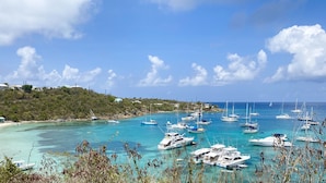 A marina with multiple boats docked, clear turquoise water, and a hillside with buildings in the background. - Water Island Cottage with a View  (St Thomas)