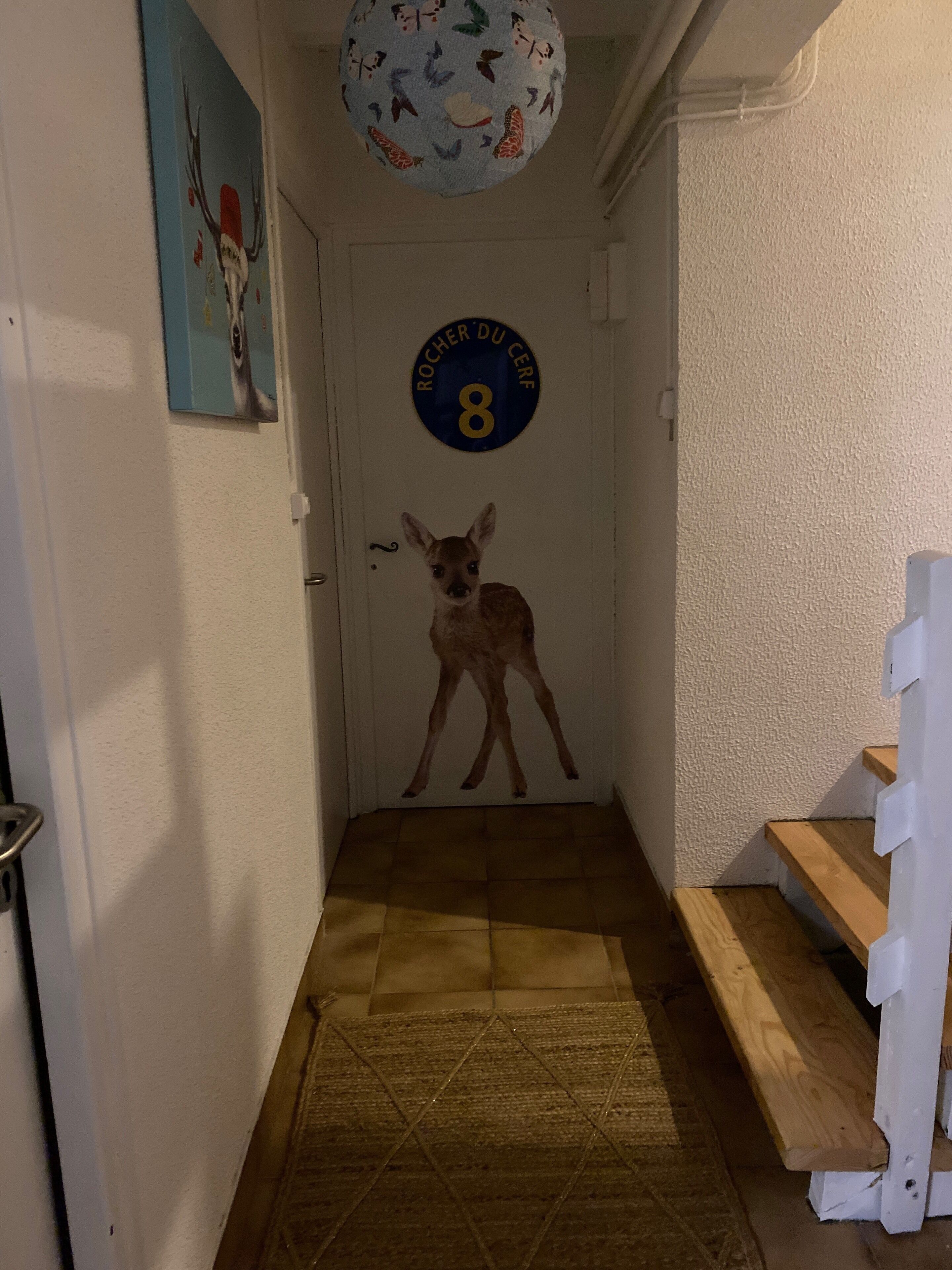 Un couloir avec un banc en bois, une porte portant un numéro et un luminaire au plafond.