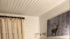 Ett sovrum med en säng, en inramad bild av en katt, en lampa och en vägghylla med en målning av ett rådjur.