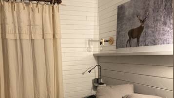 A bedroom with a bed, a framed picture of a cat, a lamp, and a wall-mounted shelf with a deer painting.