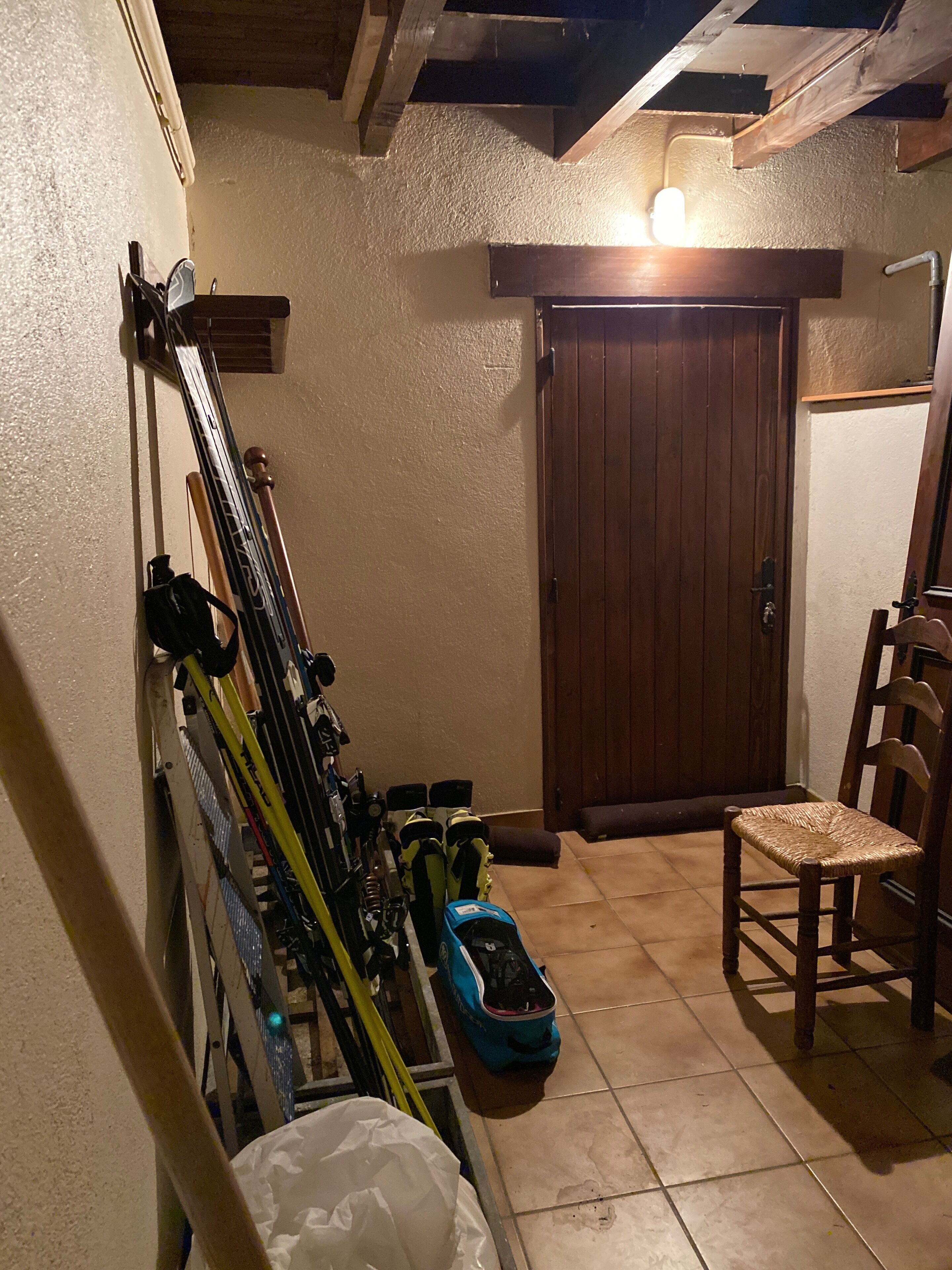 Ein Zimmer mit Holztür, einem Stuhl und Ski, die an der Wand lehnen.