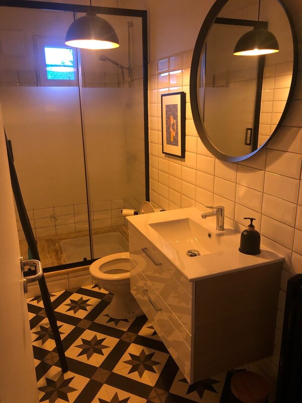 A bathroom with a white sink, a mirror, a toilet, and a shower area.
