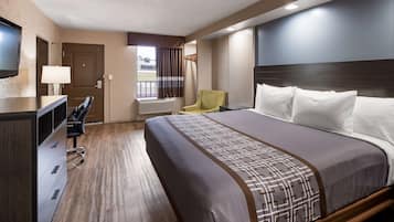 A hotel room with a large bed, a desk with a chair, a television, and a window with curtains.