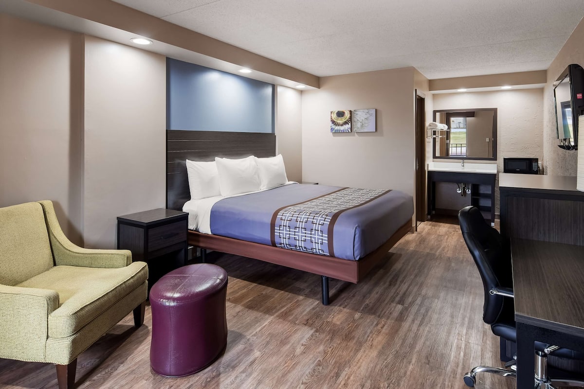 Una habitación de hotel con una cama, una silla, un taburete pequeño, un escritorio y un espejo.