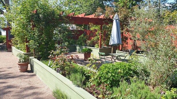 Un patio jardín con una pérgola roja, una mesa y sillas, y un paraguas grande.