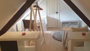 Un dormitorio tipo loft con techo inclinado, vigas de madera, una cama con cabecera blanca, una mesita y una silla.
