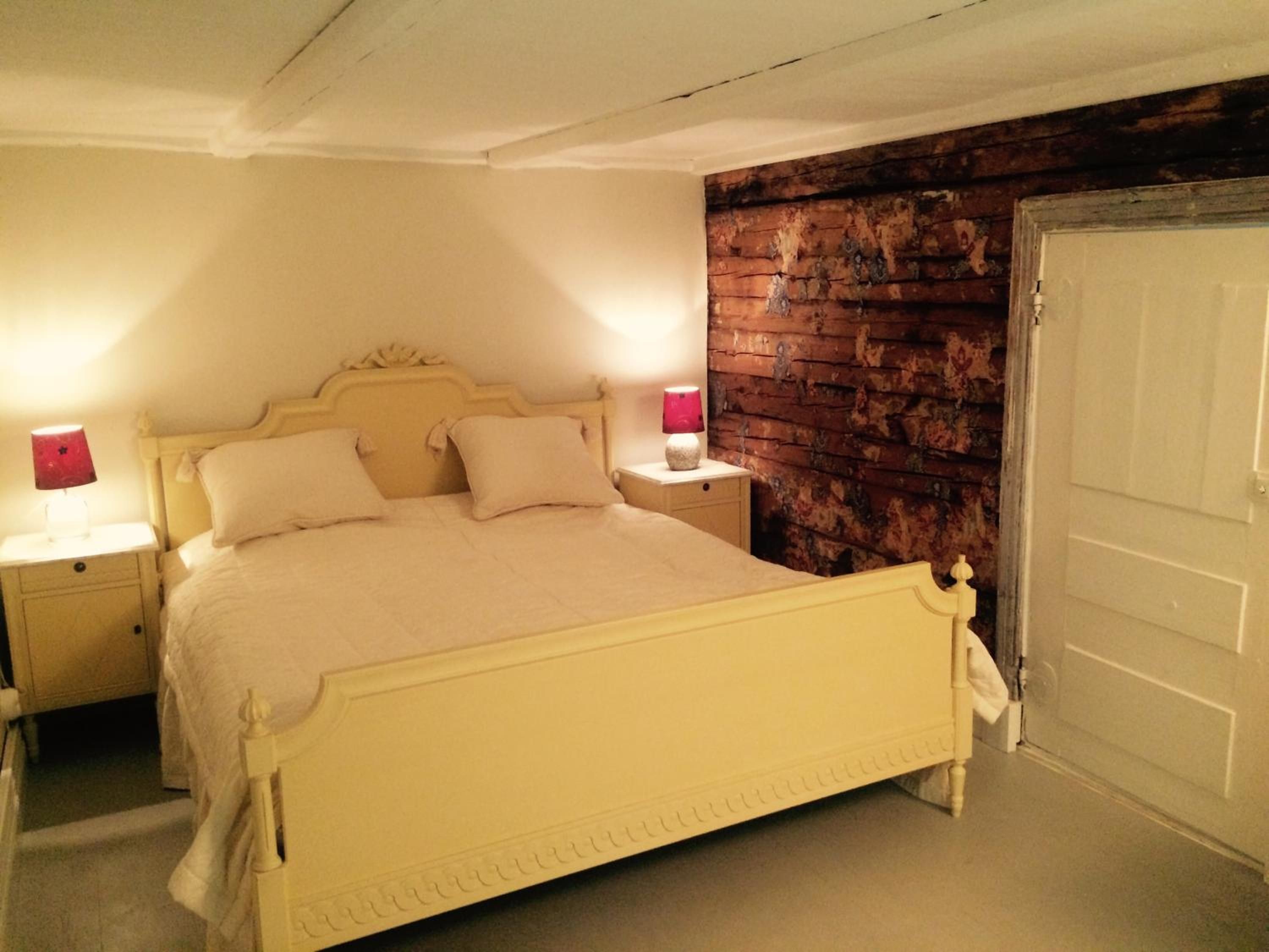 Una cama con cabecera, dos mesitas de noche con lámparas, una pared de madera y una puerta.