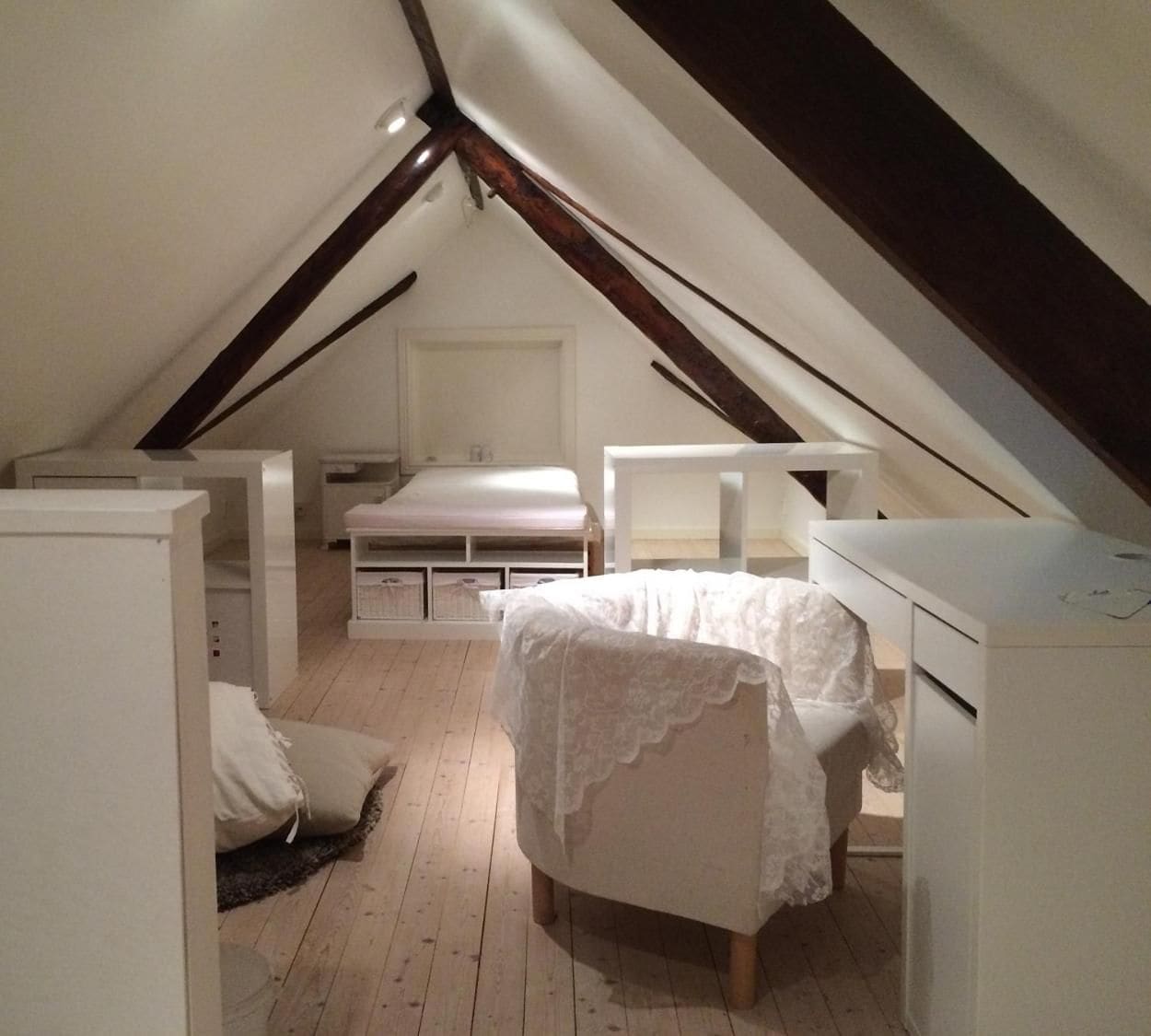 A small, attic-style bedroom with a sloped ceiling, a single bed, a chair, and a desk.