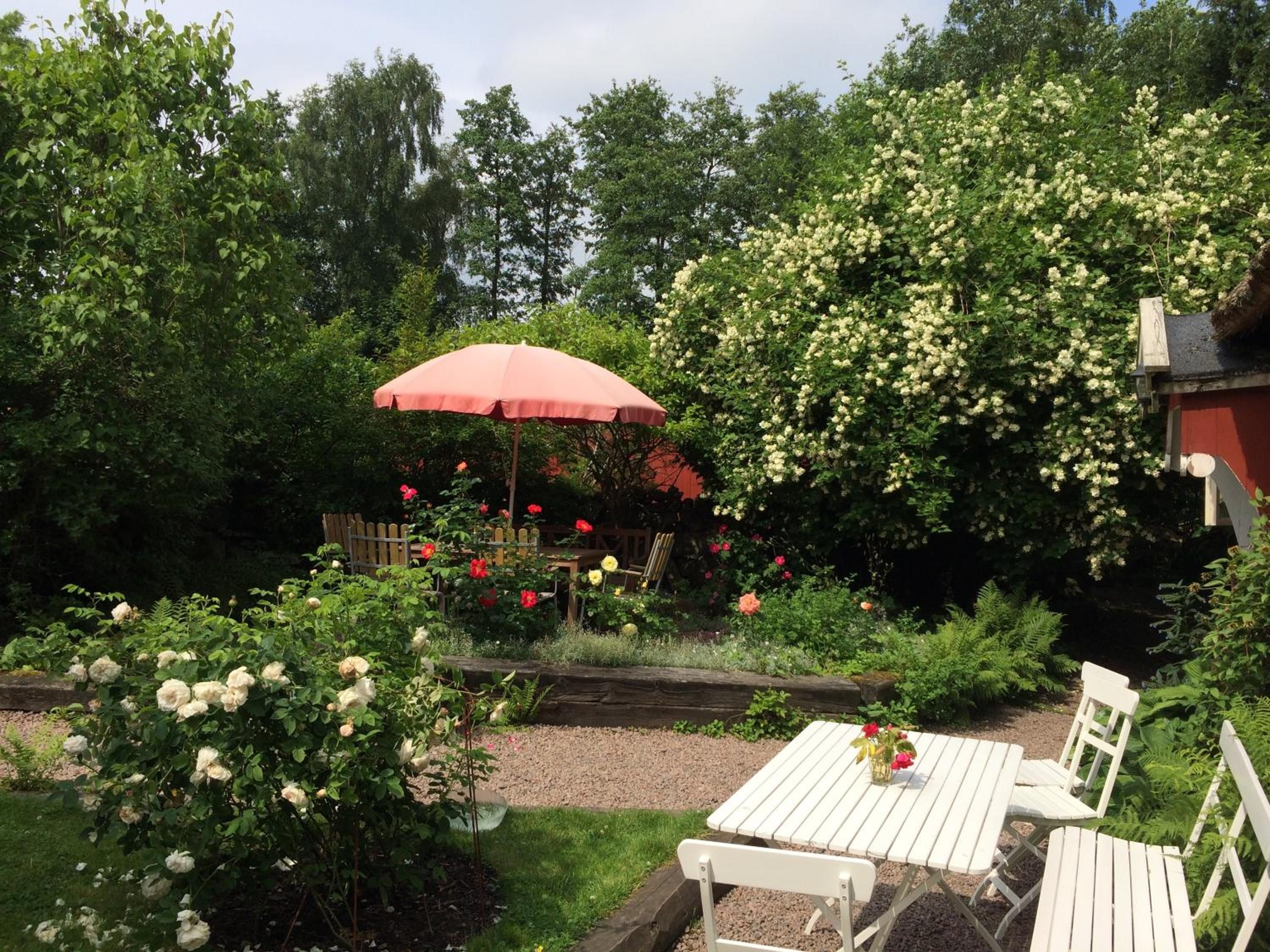 En trädgård med ett träbord och stolar, omgiven av frodig grönska och blommande växter.