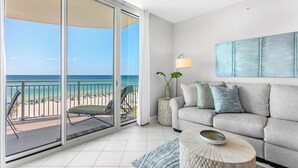 Una habitación con balcón que da a la playa, un sofá, una lámpara y un jarrón decorativo.