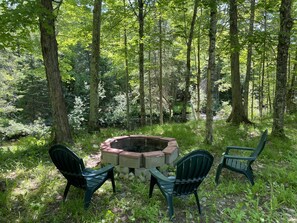 A circular fire pit surrounded by four green chairs in a forested area. - Beautiful log cabin on the Pendleton Creek!  (Iron River)
