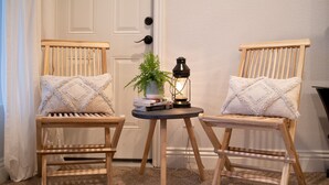 Two wooden chairs with cushioned seats and backs, a small round table with a potted plant and a lantern, and a white door in the background.