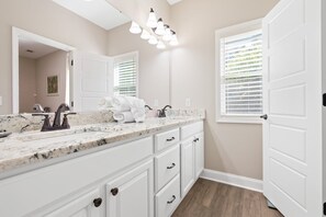 Une salle de bain avec un comptoir en marbre, des armoires blanches, un grand miroir et un luminaire au plafond.