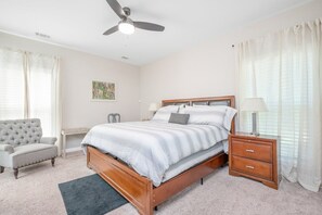 Une chambre à coucher avec un lit en bois, un bureau, une chaise, une table de chevet et un ventilateur de plafond.