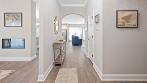 A hallway with a wooden floor, a rug, a blue chair, and framed artwork on the walls. - Gorgeous new home, one level & convenient location (Brunswick)