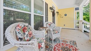A porch with wicker chairs and a small table, a yellow wall, and a decorative sign. - Gorgeous new home, one level & convenient location (Brunswick)