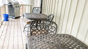 En overdækket terrasse med metalborde og -stole, grill og en blå spand.