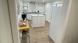 Et moderne køkken med hvide skabe, en central ø og et spiseområde med et gult bord.