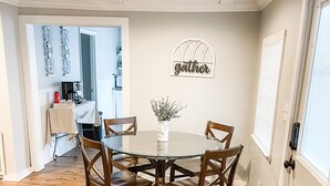 Spisestue med et rundt bord, fire træstole, en vase med blomster og et skilt med teksten 'gather' på væggen.