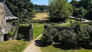 A stone building with a gravel path leading to a gate, surrounded by lush greenery and trees. - Waterfront manor house with heated pool (Baden)