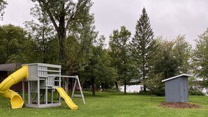 A playground with a slide and swing set, a small shed, and a grassy area with trees. - 5 bedroom 3- bath 8 people capacity pontoon included in Winter Wis. (Winter)