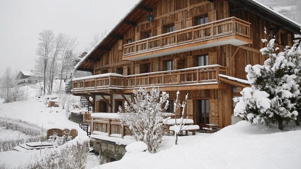 A wooden chalet with a balcony, surrounded by snow-covered trees and a snowy landscape. - Luxury apartment 14 people, with a nice view (Haute-Savoie)