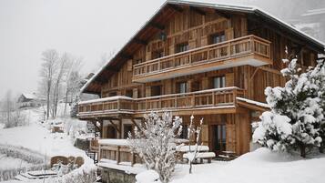 Un chalet en bois doté d’un balcon, entouré d’arbres couverts de neige et offrant une vue sur un paysage enneigé.