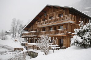 Een houten chalet met balkon, omringd door sneeuwbedekte bomen en een besneeerd landschap.