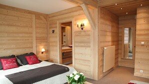 A wooden cabin bedroom with a bed, bedside lamps, a mirror, and a small table with a vase of flowers. - Luxury apartment 14 people, with a nice view (Haute-Savoie)