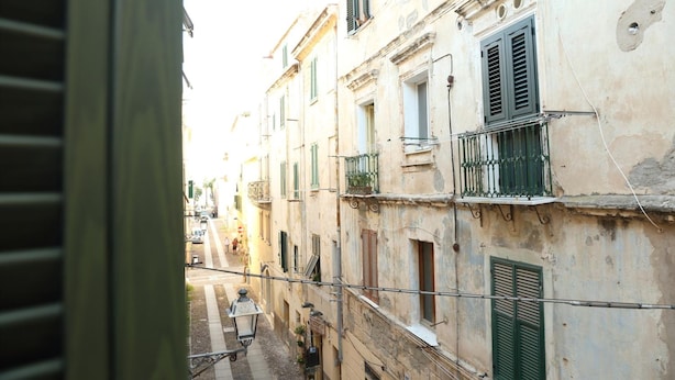 Une rue étroite bordée de vieux bâtiments, dont certains sont dotés de balcons et de volets.