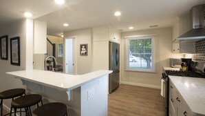 A modern kitchen with a central island, stainless steel appliances, and a view of the street through the window. - Centrally Located DoCo Oasis (Fish Creek)
