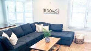 A modern living room with a dark sectional sofa, a wooden coffee table, and a woven rug. - Centrally Located DoCo Oasis (Fish Creek)