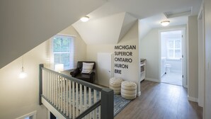A spacious hallway with a sloped ceiling, a staircase with a white railing, and a door leading to a bathroom. - Centrally Located DoCo Oasis (Fish Creek)