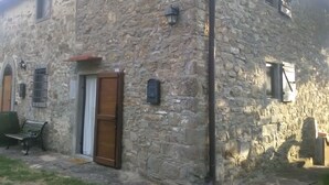 Ein Steinhaus mit einer Holztür, einer Bank und einem kleinen Fenster.