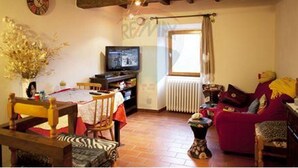 Ein gemütliches Wohnzimmer mit Holzboden, einem Fernseher, einem Esstisch mit Stühlen und einem roten Sofa.