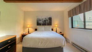 A bedroom with a large bed, two bedside tables with lamps, a dresser, a window with curtains, and a painting on the wall. - Comfortable Condo close to Slopes with a Hot Tub! (Mt. Crested Butte)