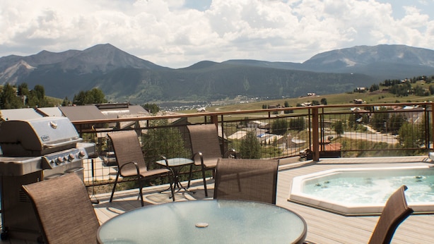 A deck with outdoor furniture, a hot tub, and a grill. - Comfortable Condo close to Slopes with a Hot Tub! (Mt. Crested Butte)